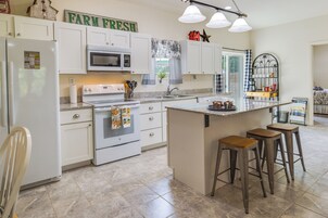 Una cocina moderna con armarios blancos, una isla central con taburetes, microondas, horno y refrigerador.