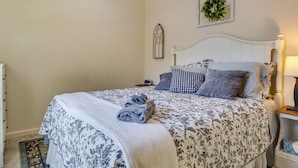 Una cama bien hecha con colcha floral, cabecera blanca y mesita de noche con lámpara.