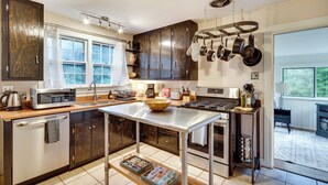 A modern kitchen with dark wooden cabinets, a stainless steel countertop, and a hanging pot rack. - Hendersonville Haven w/ Fire Pit, Grill, Deck! (Hendersonville)