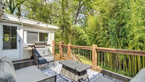 A covered outdoor deck with seating and a barbecue area, surrounded by lush greenery. - Hendersonville Haven w/ Fire Pit, Grill, Deck! (Hendersonville)