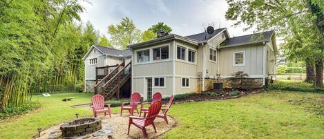 A two-story house with a backyard featuring a fire pit and red Adirondack chairs.