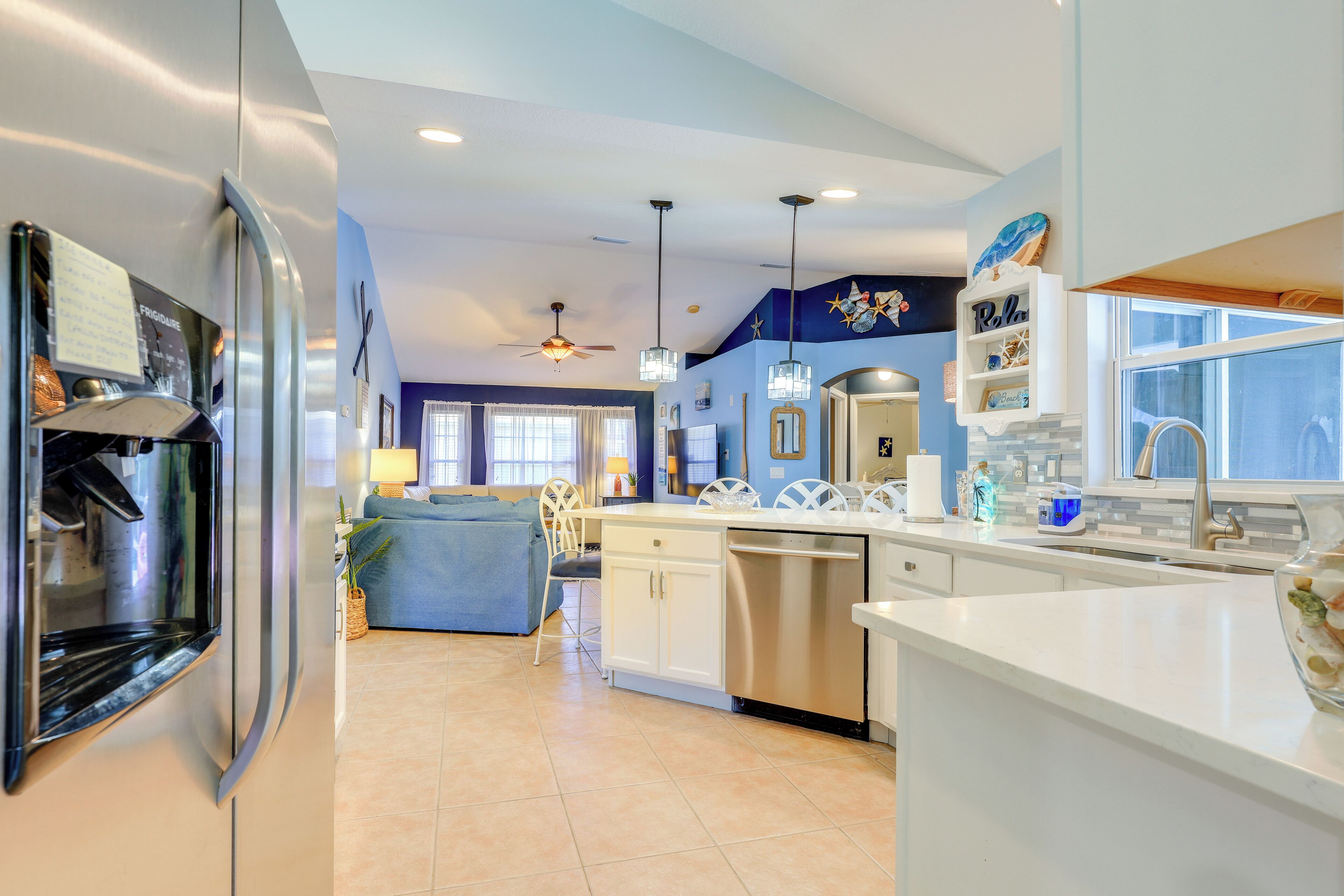 A modern kitchen with a refrigerator, dishwasher, and a dining area with a blue sofa and chairs.