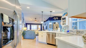 A modern kitchen with a refrigerator, dishwasher, and a dining area with a blue sofa and chairs. - Jensen Beach Home w/ Heated Pool! (Jensen Beach)
