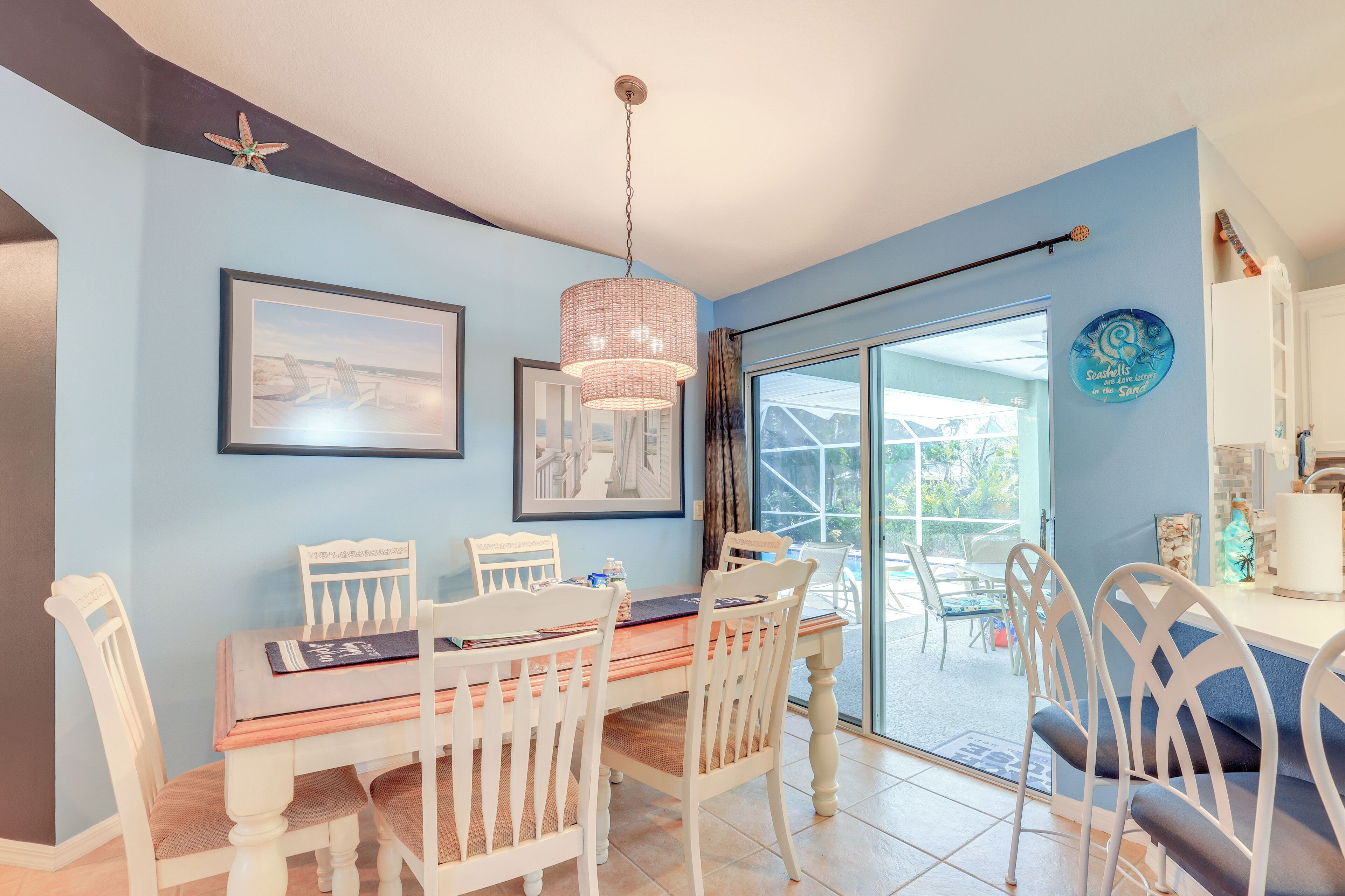A dining area with a table and chairs, a hanging light fixture, and a view through a glass door to the outside.