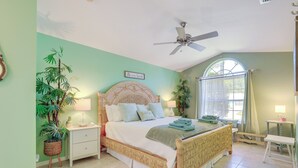 A bedroom with a bed, nightstands, a ceiling fan, a window with curtains, and potted plants. - Jensen Beach Home w/ Heated Pool! (Jensen Beach)