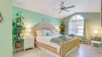 A bedroom with a bed, nightstands, a ceiling fan, a window with curtains, and potted plants.