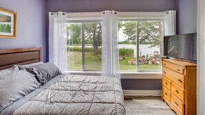 Un dormitorio con una cama, un aparador, un televisor y un ventanal con cortinas.