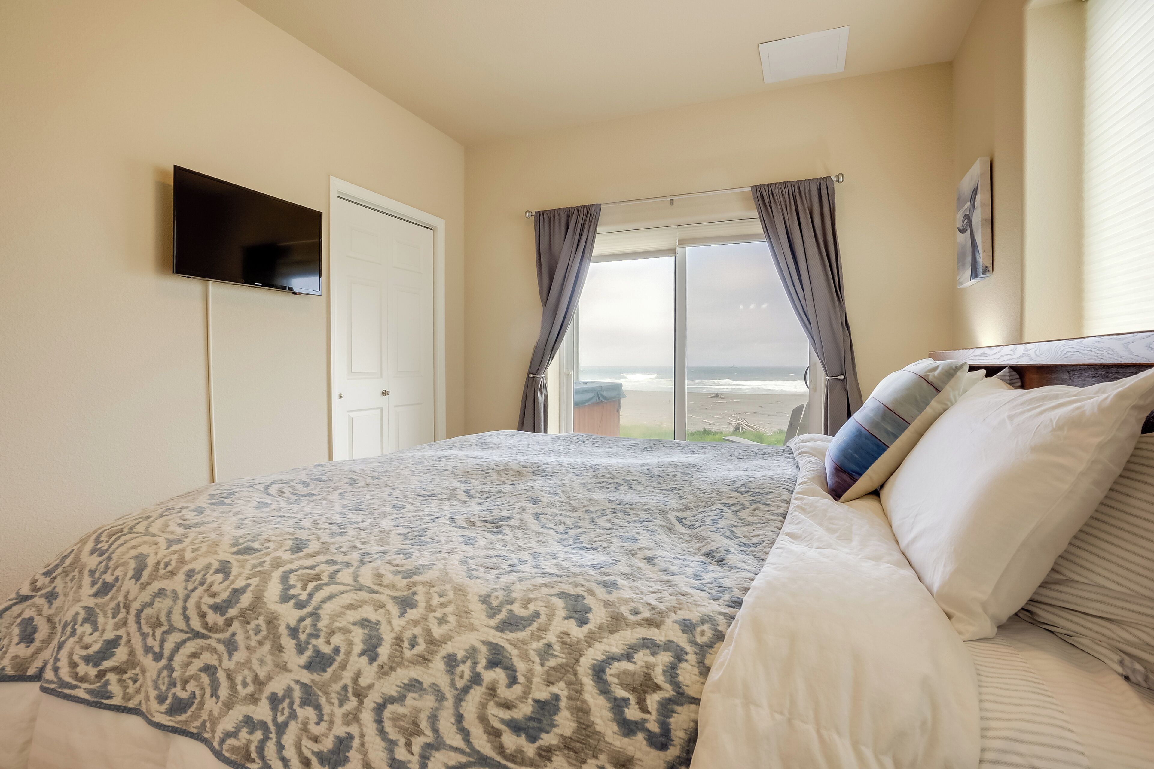 A bedroom with a bed, a television on the wall, and a window with curtains.