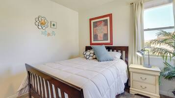 A bedroom with a wooden bed, a nightstand with drawers, a lamp, a window with curtains, and wall decorations.