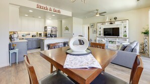 Une cuisine moderne avec des meubles blancs, une table à manger avec des chaises, un lustre et un coin salon avec un canapé et un téléviseur.
