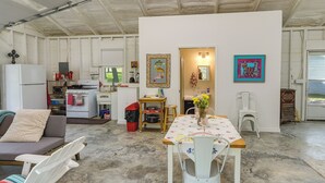 A compact kitchen with a refrigerator, stove, and sink. There is a dining area with a table and chairs, and a sofa with a striped cushion. - Coffeyville Countryside Studio w/ Fire Pit! (Coffeyville)