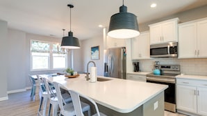 A modern kitchen with white cabinets, stainless steel appliances, and a central island with bar stools. - Beaufort Getaway w/ Pool Access, 2 Mi to Downtown! (Beaufort)