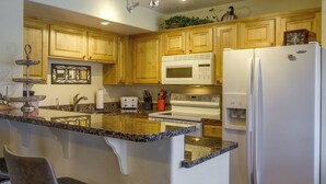 Une cuisine avec des meubles en bois, un plan de travail en granit, un réfrigérateur blanc et un four à micro-ondes.
