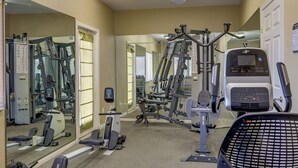 Une salle de sport équipée de divers appareils d’exercice, de miroirs et d’un ventilateur au plafond.