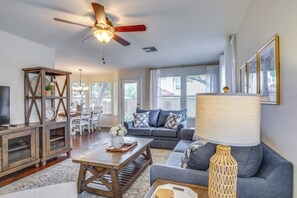 A spacious living room with a ceiling fan, a sofa set, a coffee table, a TV, and a dining area with chairs and a table.