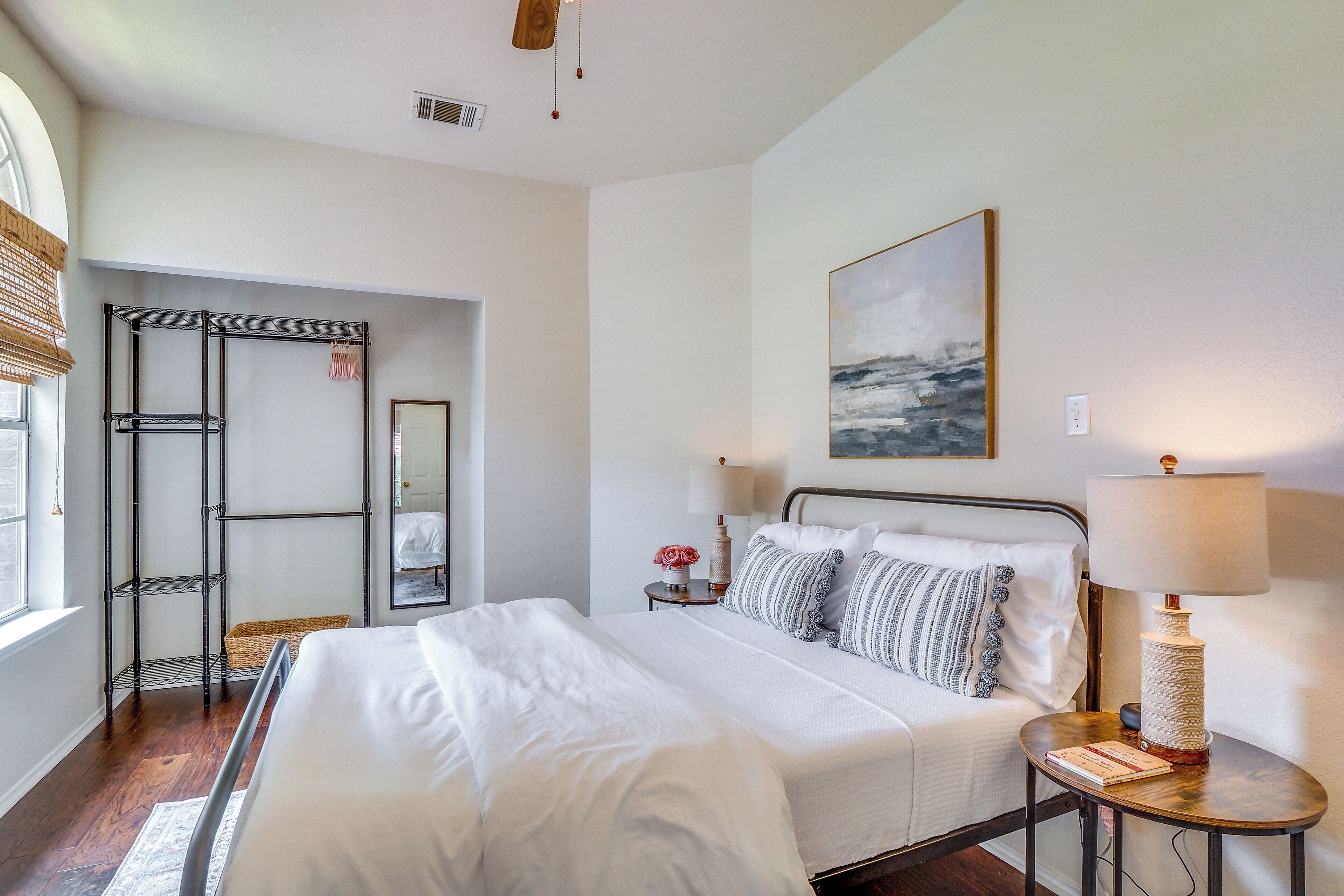 Une chambre à coucher bien rangée, avec un grand lit, des tables de chevet, un portant et un tableau accroché au mur.