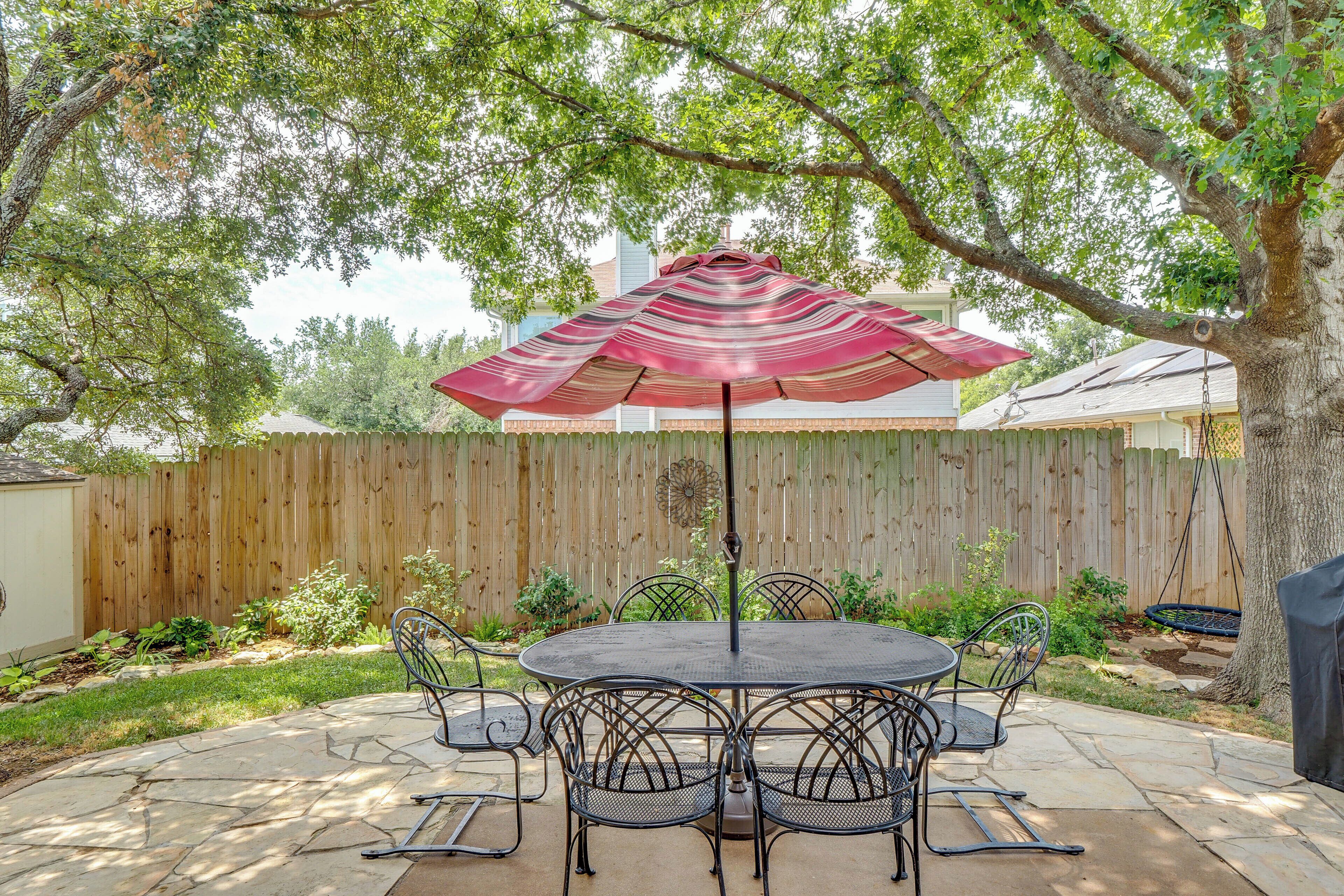 A patio with a round table and chairs, an umbrella, and a wooden fence in the background.