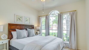 A bedroom with a large bed, a wooden headboard, two bedside tables with lamps, a ceiling fan, and a window with curtains. - Fenced Yard + Patio: Family Home in Round Rock (Round Rock)