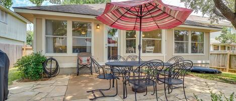 A patio with a stone floor, a table with chairs, and a red umbrella.