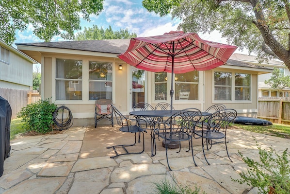 A patio with a stone floor, a table with chairs, and a red umbrella.