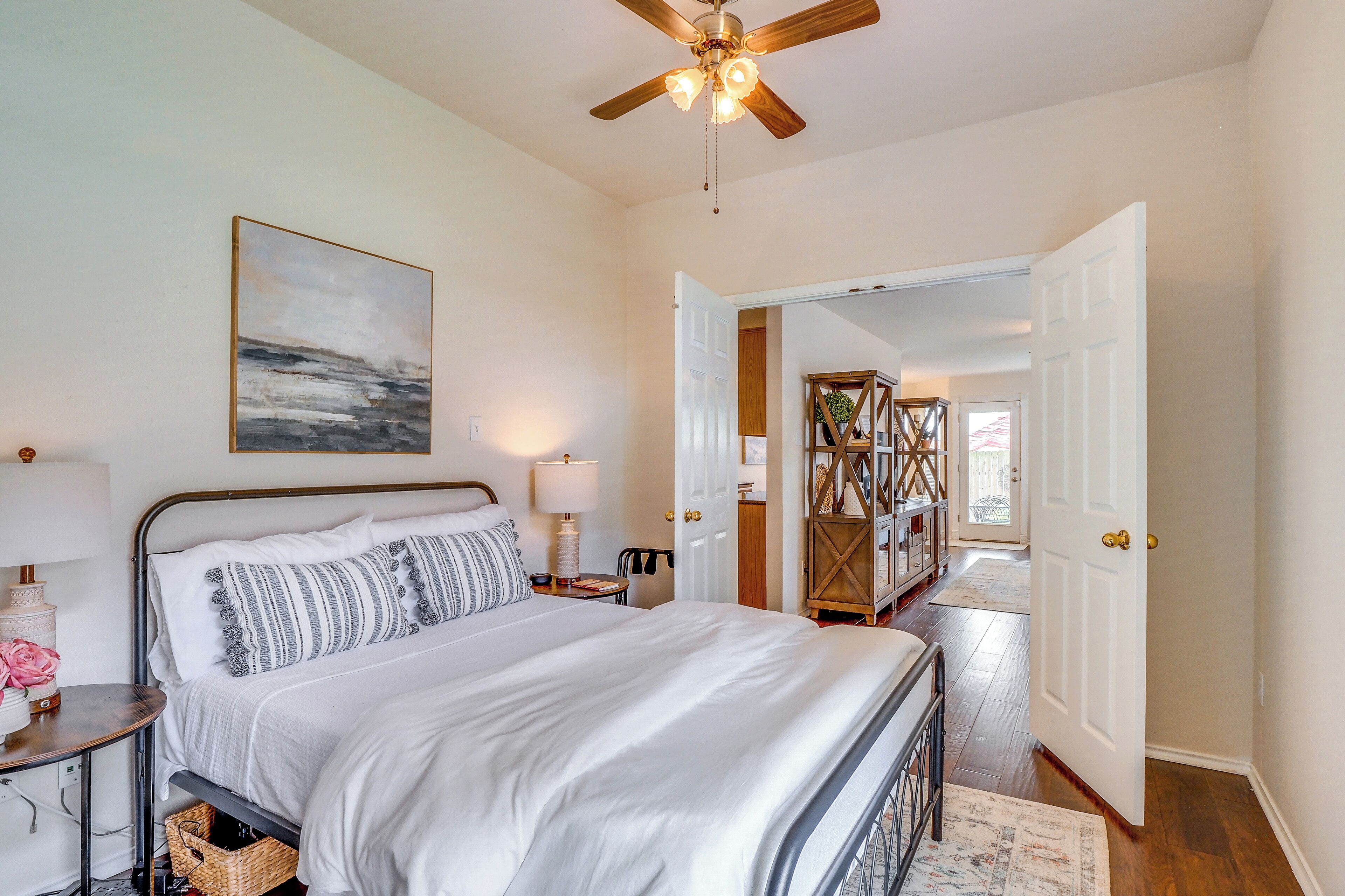 A bedroom with a bed, bedside tables, a ceiling fan, and a door leading to another room.