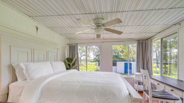 A bedroom with a large bed, a ceiling fan, and a view of the outdoors.