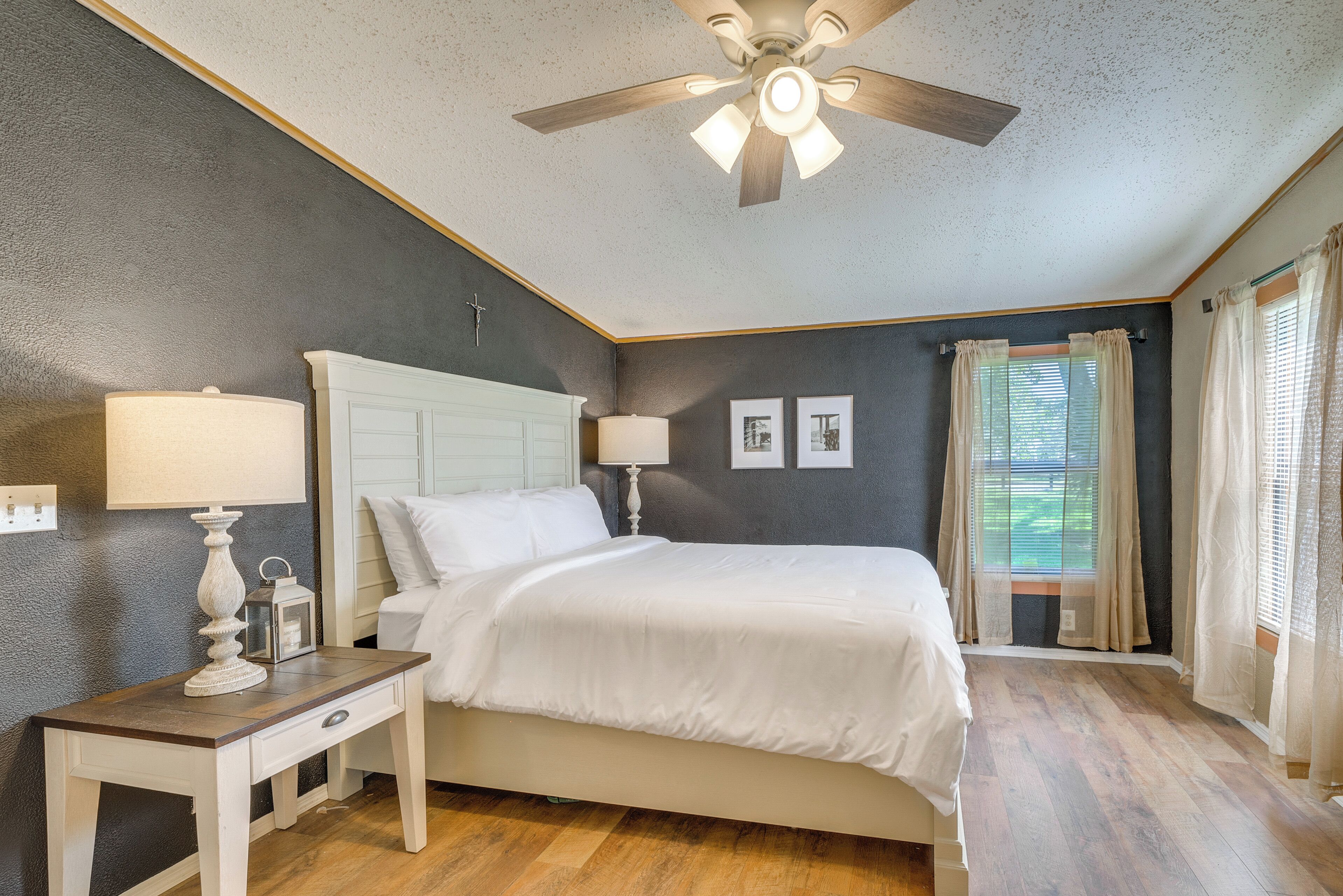 A bedroom with a bed, bedside lamps, a nightstand, a ceiling fan, and a window with curtains.