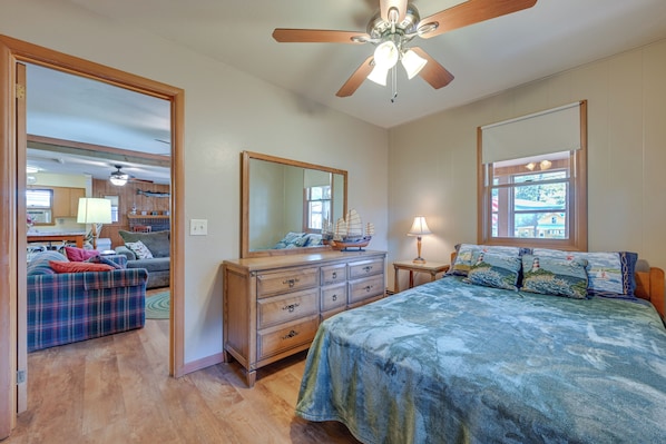 A bedroom with a bed, dresser, mirror, and a view of the living area.