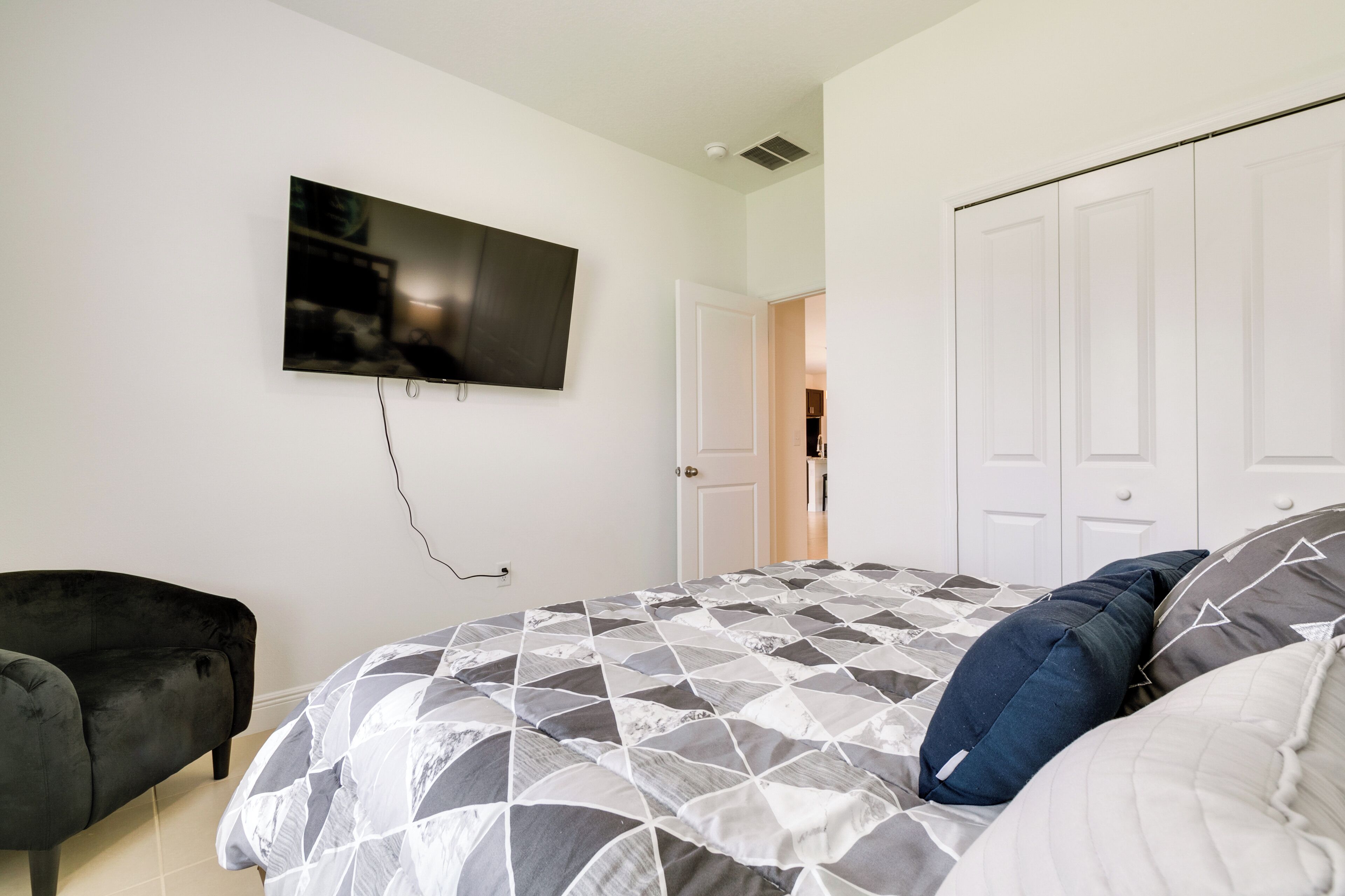 Een slaapkamer met een bed, een aan de muur bevestigde televisie, een deur en een stoel.
