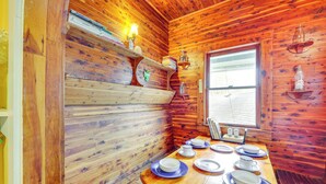 A wooden cabin interior with a dining table set for four, a window with blinds, and wooden walls. - Eureka Springs Vacation Rental < Half-mi to Dtwn! (Eureka Springs)