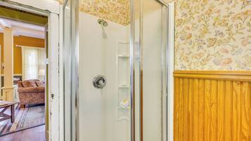 A room with a shower, a wooden panel wall, and a floral wallpaper pattern.