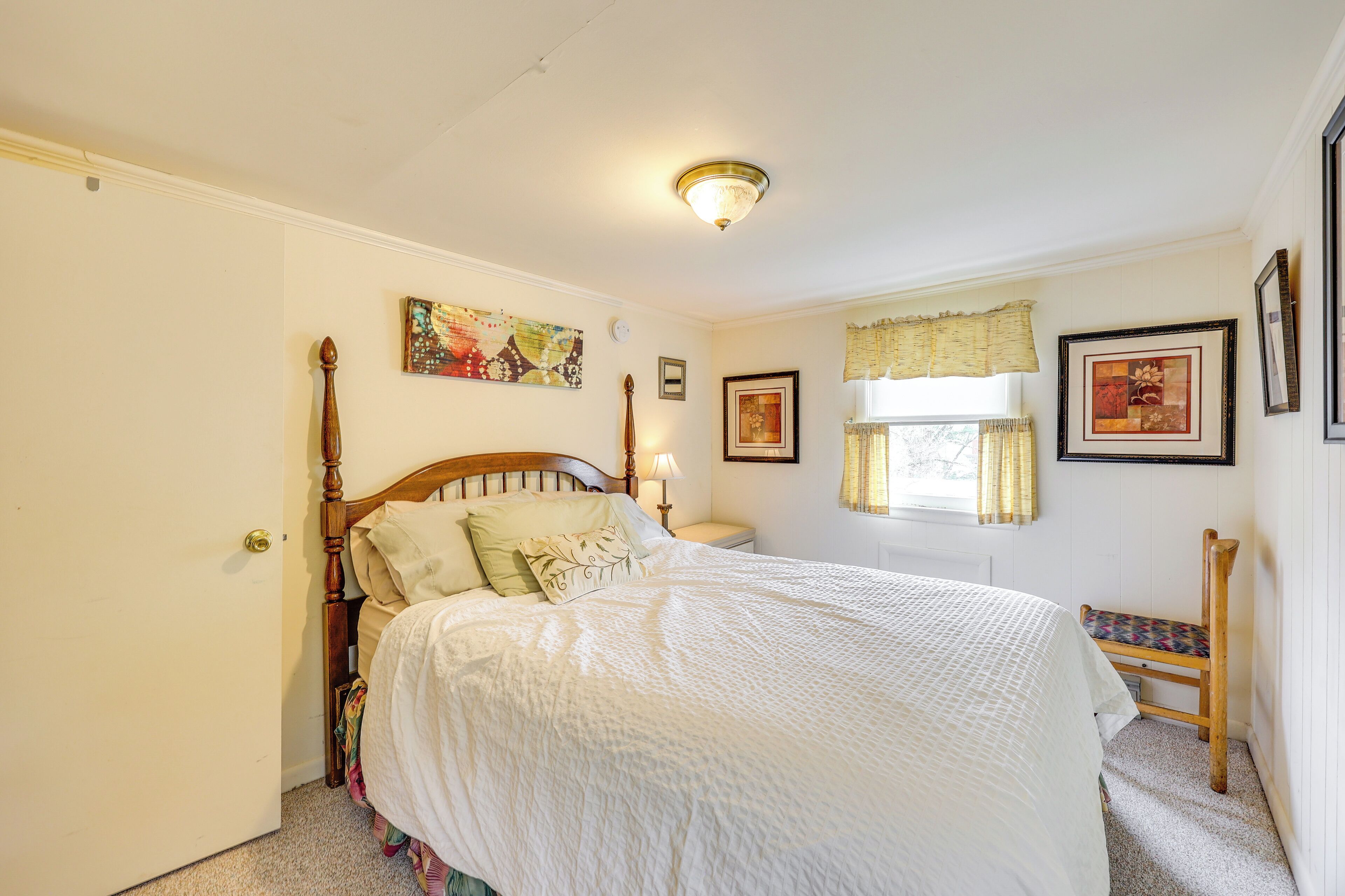 Un dormitorio con cama de madera, una mesita de noche, una silla y un ventanal con cortinas.