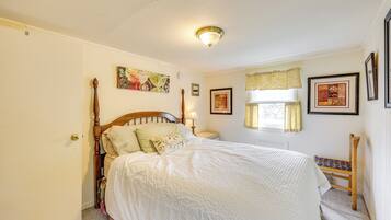 A bedroom with a wooden bed, a nightstand, a chair, and a window with curtains.