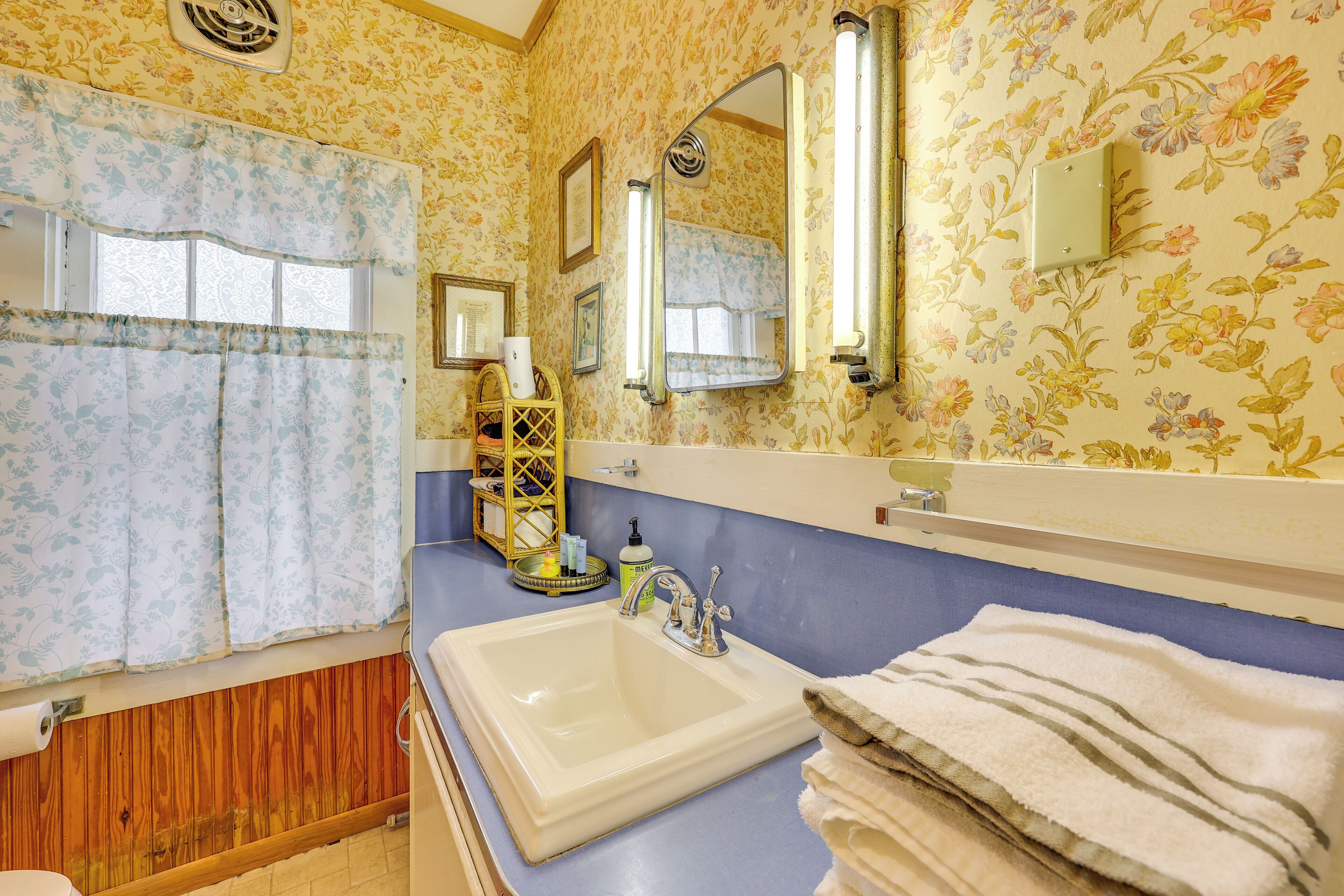A bathroom with a floral wallpaper, a sink with a mirror, and a wooden vanity.