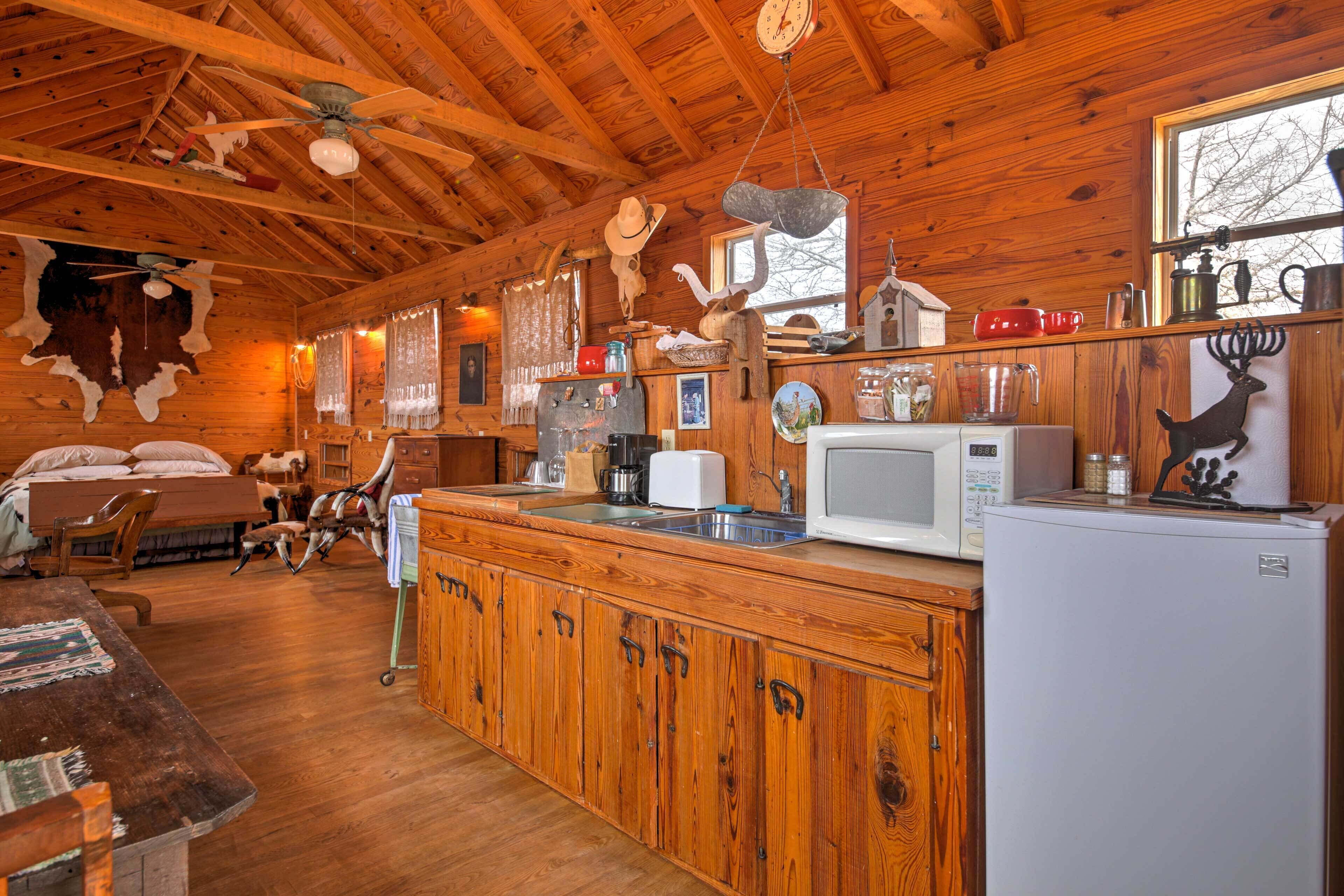 Interior rústico de una cabaña con paredes y techo de madera, una zona de cocina con refrigerador, microondas, pileta y diversos utensilios.