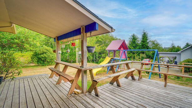 Eine Holzterrasse mit Picknicktischen und einem Spielplatz mit einer Rutsche.