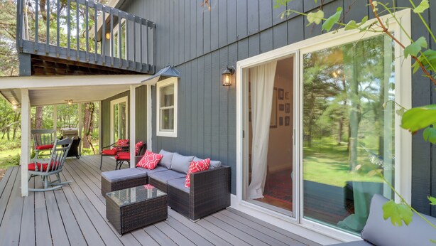 Eine überdachte Terrasse mit Korbmöbeln, eine Glastür zu einem Garten und ein Holzgeländer.