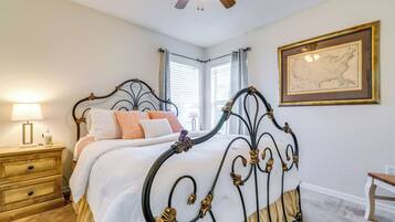A neatly arranged bedroom with a classic bed, bedside tables, a nightstand, a ceiling fan, and a framed map on the wall.