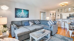 A modern living room with a grey sectional sofa, a coffee table, and a painting of an octopus on the wall. - Ocean Access & Balcony: Surfside Beach Condo (Myrtle Beach)