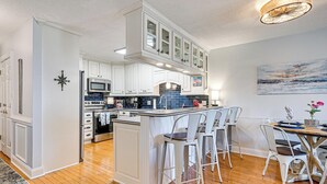 A modern kitchen with white cabinetry, a central island, and a dining area with white chairs. - Ocean Access & Balcony: Surfside Beach Condo (Myrtle Beach)