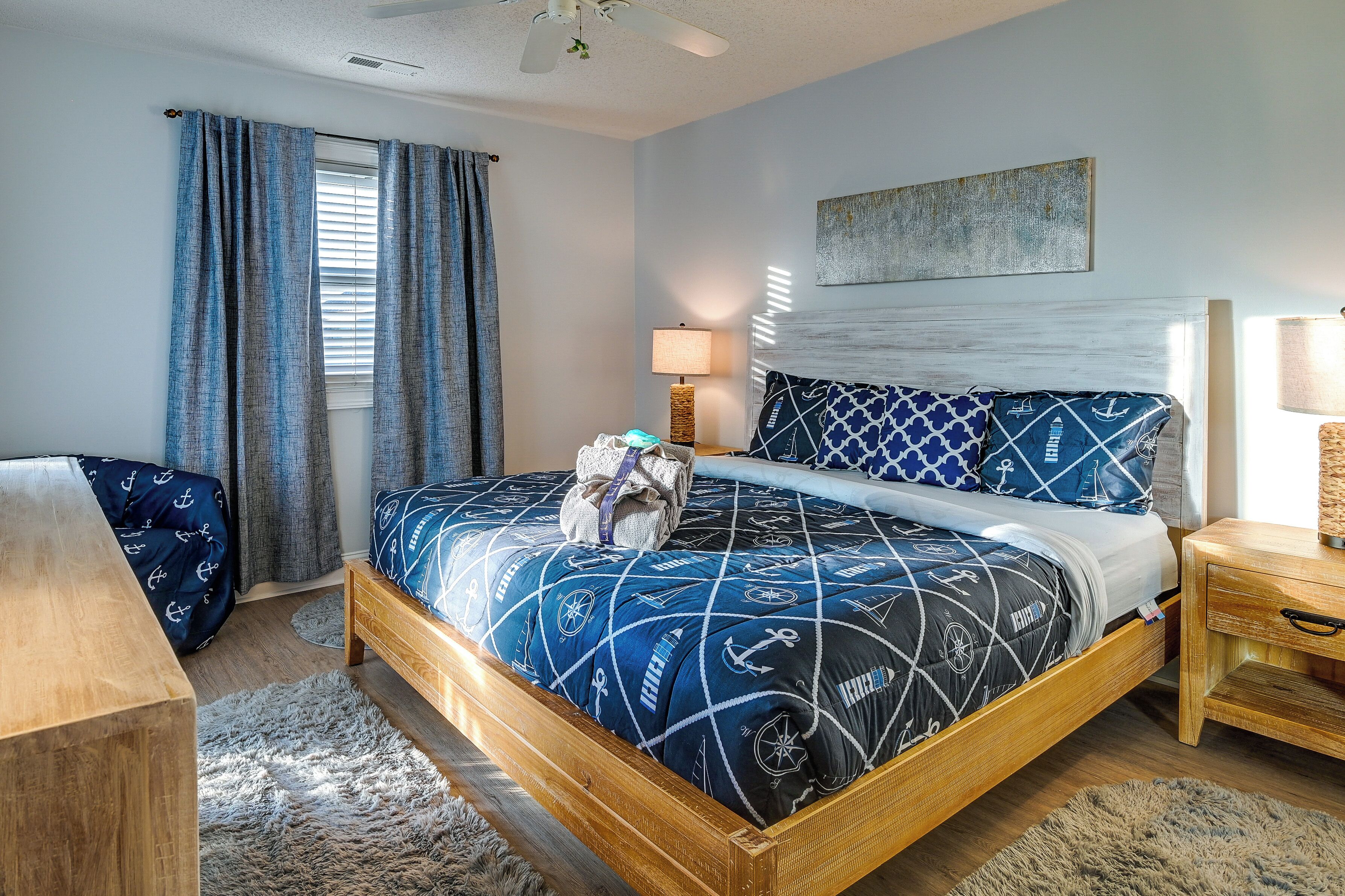 A bedroom with a bed, a wooden nightstand, a desk, and a window with curtains.
