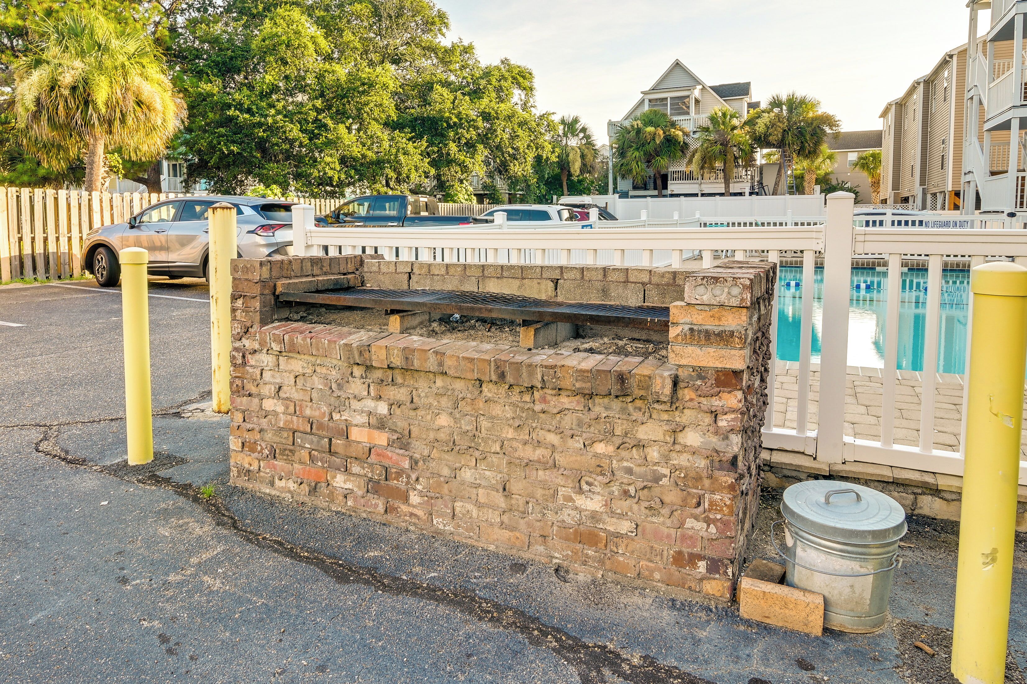 A brick wall with a metal bucket, a pool, and a white fence.
