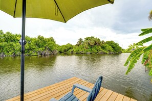 A wooden dock with a bench and a green umbrella, overlooking a calm river with dense greenery and trees.