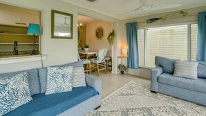 A living room with a sofa, a dining table with chairs, a ceiling fan, and a window with curtains.