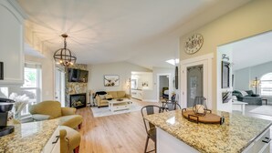 A spacious kitchen with a large island, wooden flooring, and a chandelier. There is a dining area with a table and chairs, and a living room with a sofa and a fireplace. - Coeur D'alene Vacation Rental ~ 4 Mi to the Lake! (Coeur d'Alene)