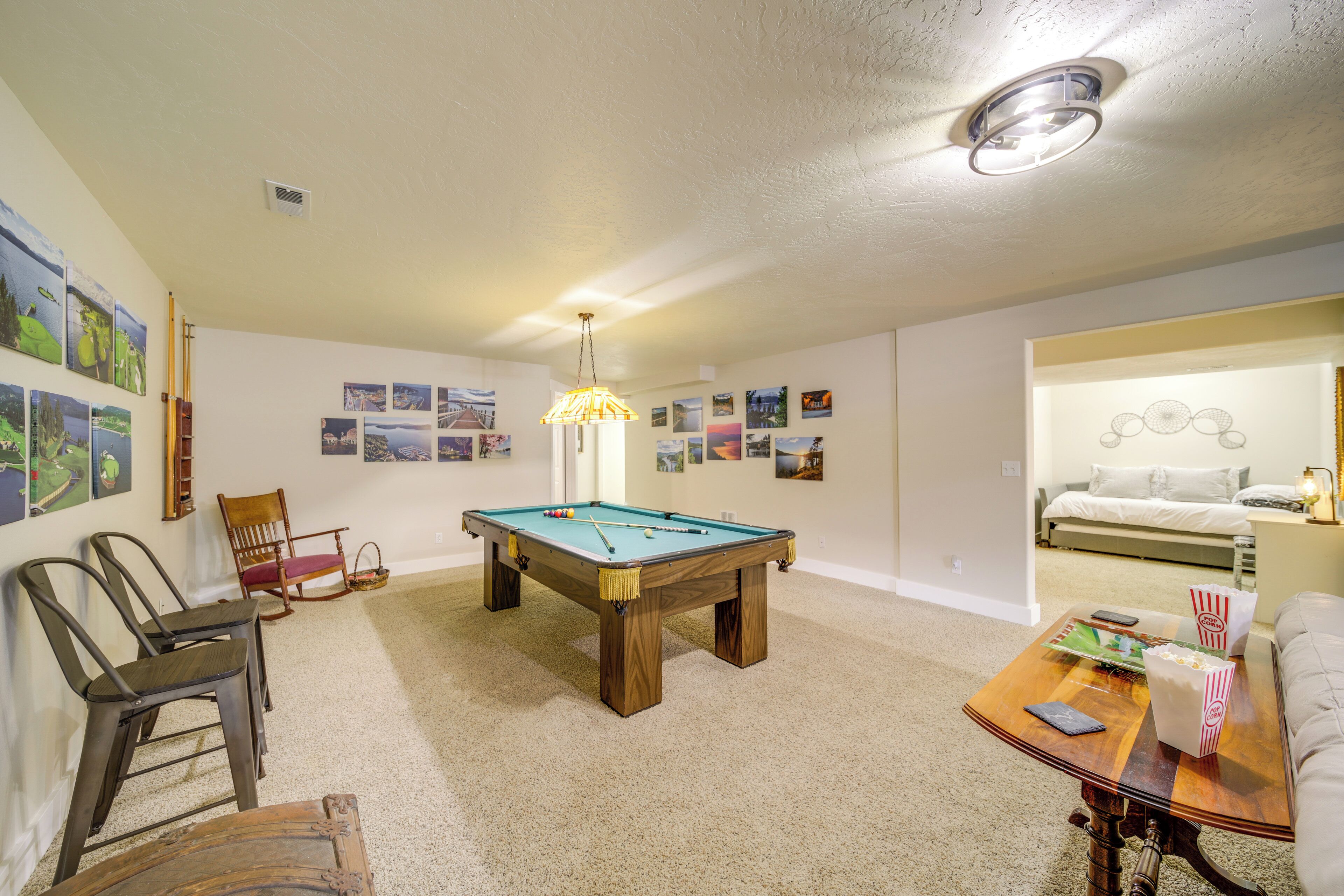 A room with a pool table, chairs, a sofa, and a coffee table with snacks.