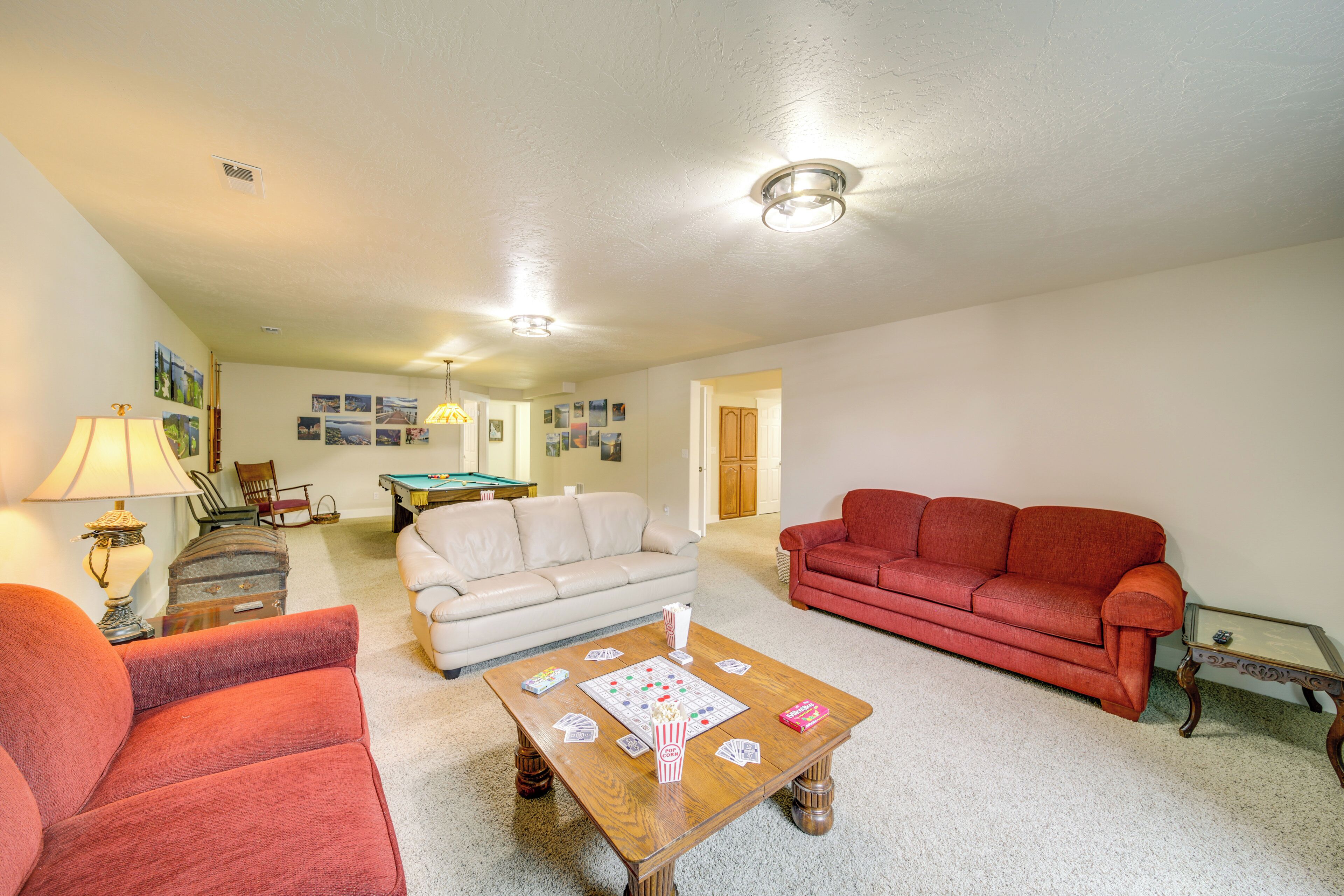 A living room with a beige sofa, a red sofa, a wooden coffee table with board games, and a lamp.