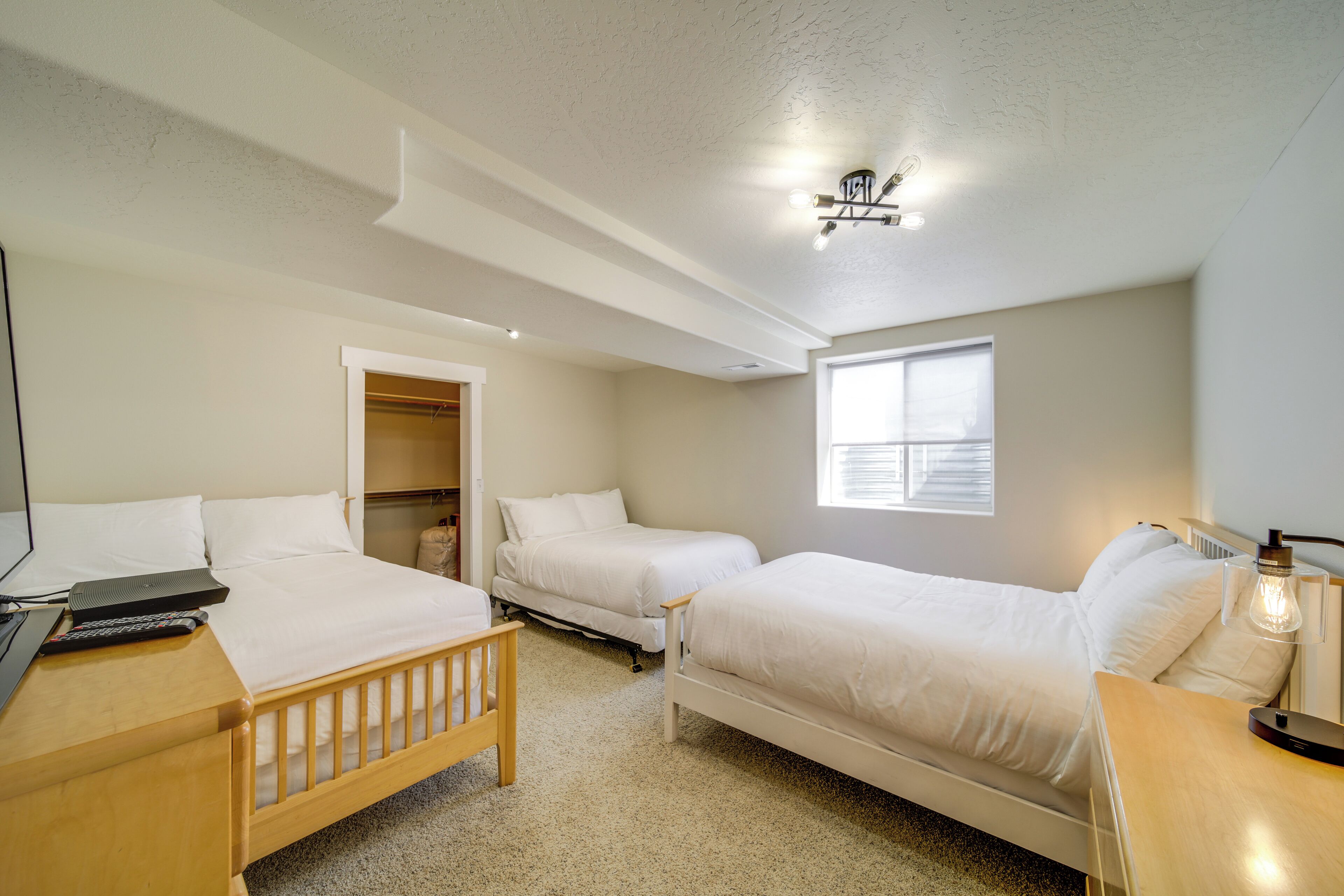 Une chambre avec deux lits simples, un bureau en bois, une chaise, une table de chevet avec une lampe et une armoire.