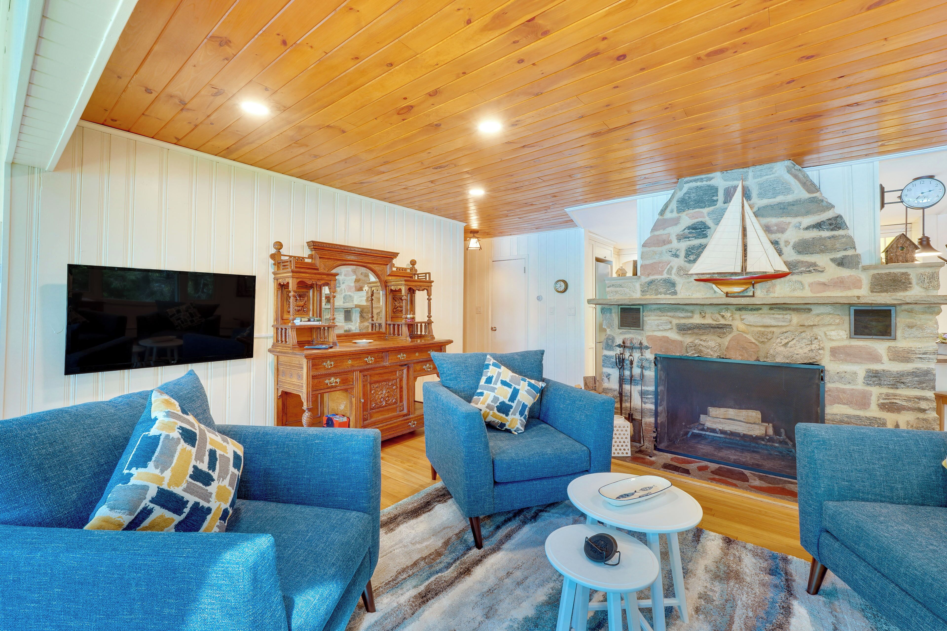 Una sala de estar acogedora con sofás azules, techo de madera, chimenea de piedra y un televisor montado en la pared.