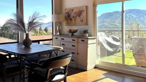 Ein Zimmer mit großem Fenster und Blick auf die Berge, einem Esstisch mit Stühlen, einer weißen Kommode mit Schubladen und einem dekorativen Globus an der Wand.